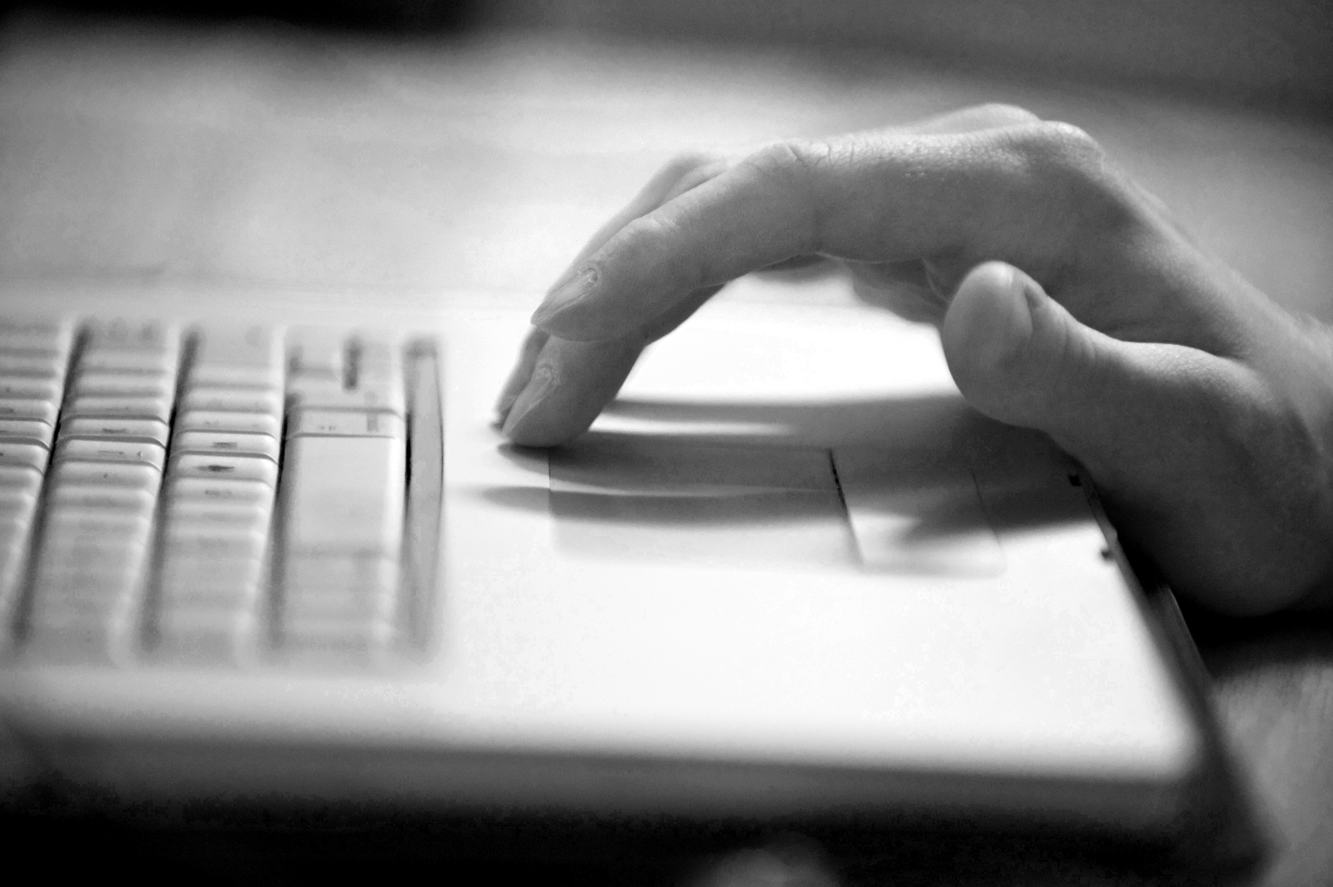 Black and white photo of a hand using the mouse trackpad on a laptop