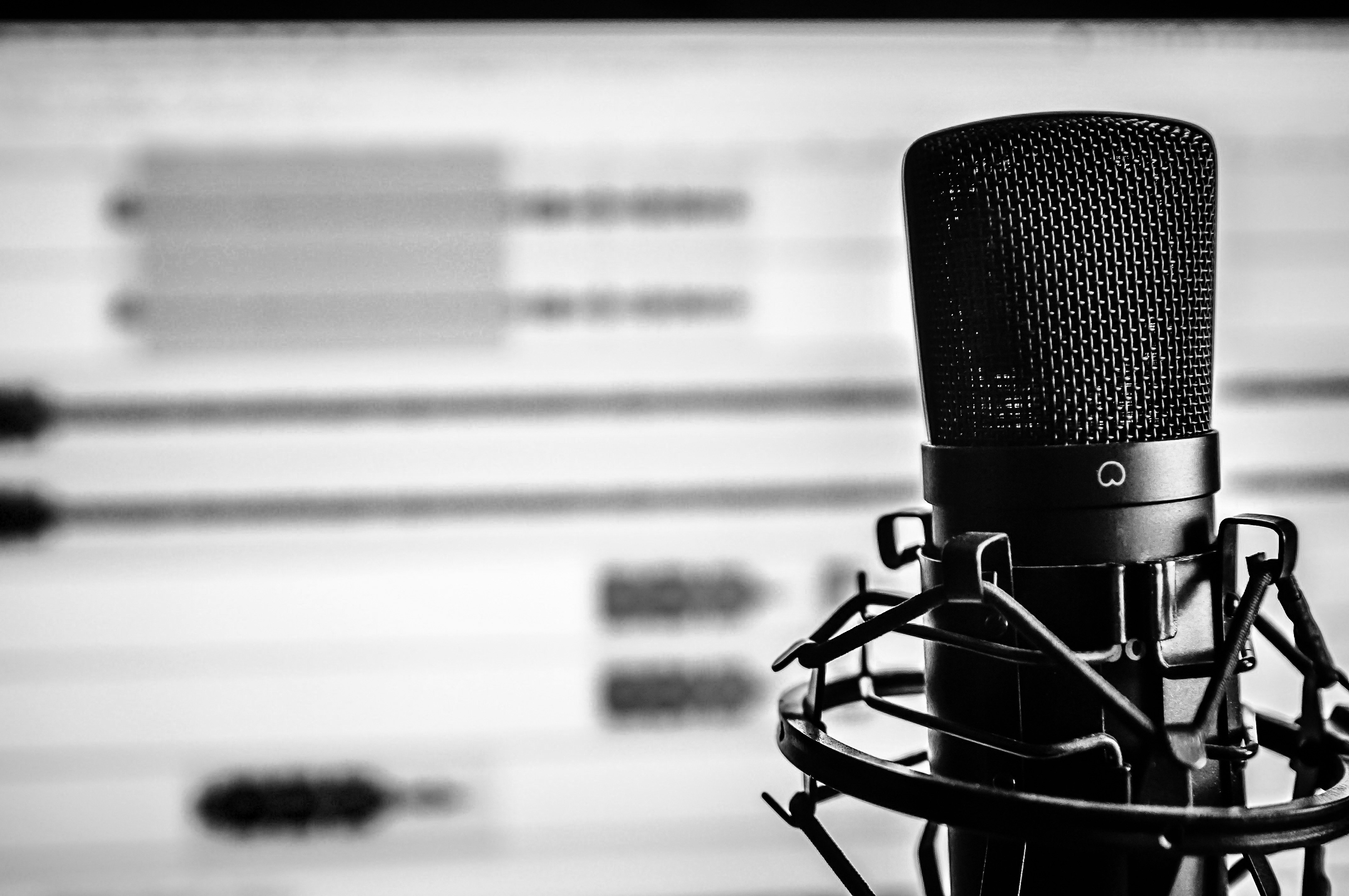 Black and White photo of a microphone in front of a computer monitor showing audio editing software