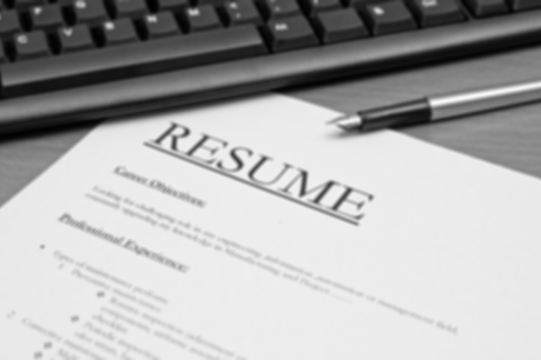 Black and white image of a resume on a desk near a computer keyboard and a fountain pen